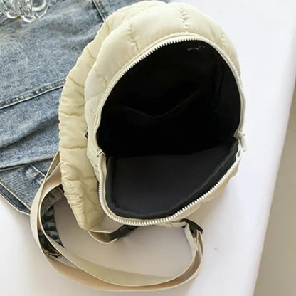 Open cream quilted sling bag showing black interior lining, displayed on denim jacket background