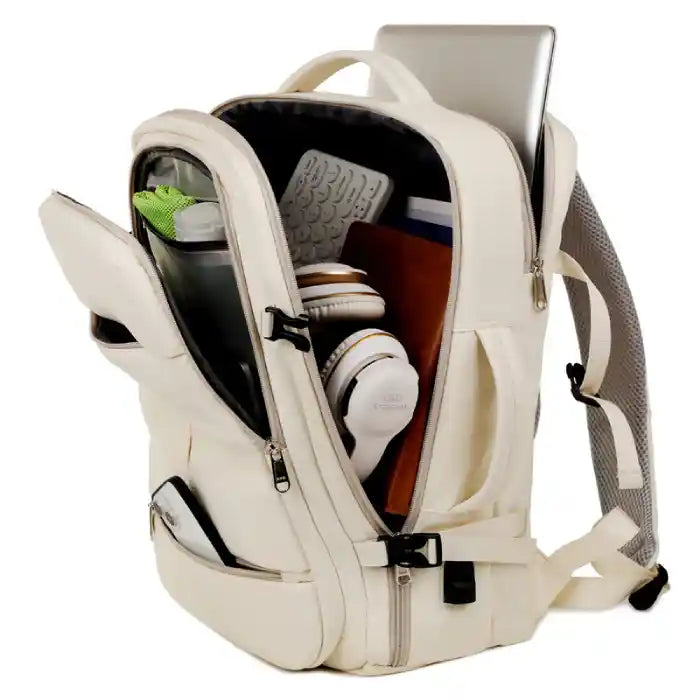 Open cream backpack showing large organized storage with tech gadgets, books, and laptop compartment.