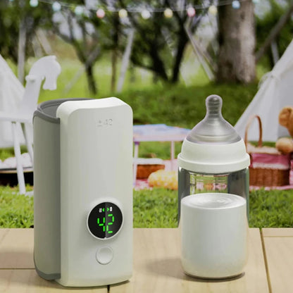 Portable bottle warmer and baby bottle on wooden table outdoors, picnic setting with string lights and trees in background