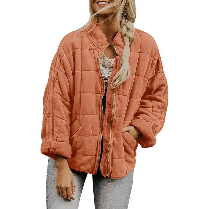 Oversized quilted zip jacket in orange with collarless neckline and square quilting, front view.