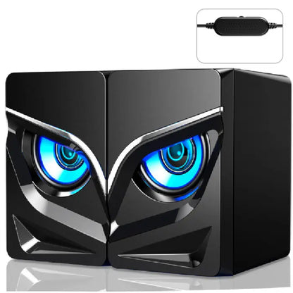 Black computer speakers with owl-like blue glowing eyes, angular design, and USB controller