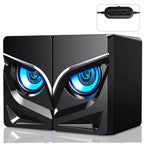 Black computer speakers with owl-like blue glowing eyes, angular design, and USB controller