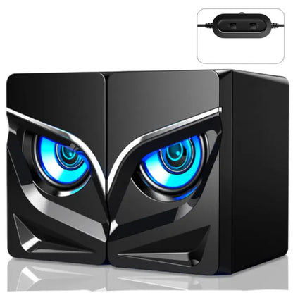 Black computer speakers with owl-like blue glowing eyes, angular design, and USB controller