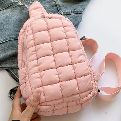 Pastel pink quilted sling bag with zipper closure and adjustable strap, displayed on denim jacket background