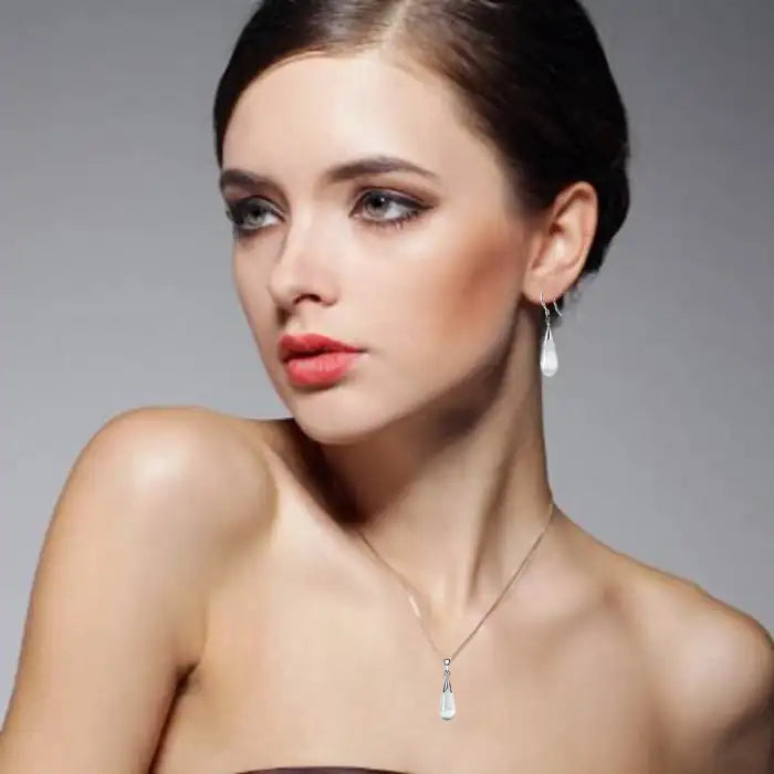 Pendant necklace earrings combo worn by model with sleek hair and subtle makeup against gray background