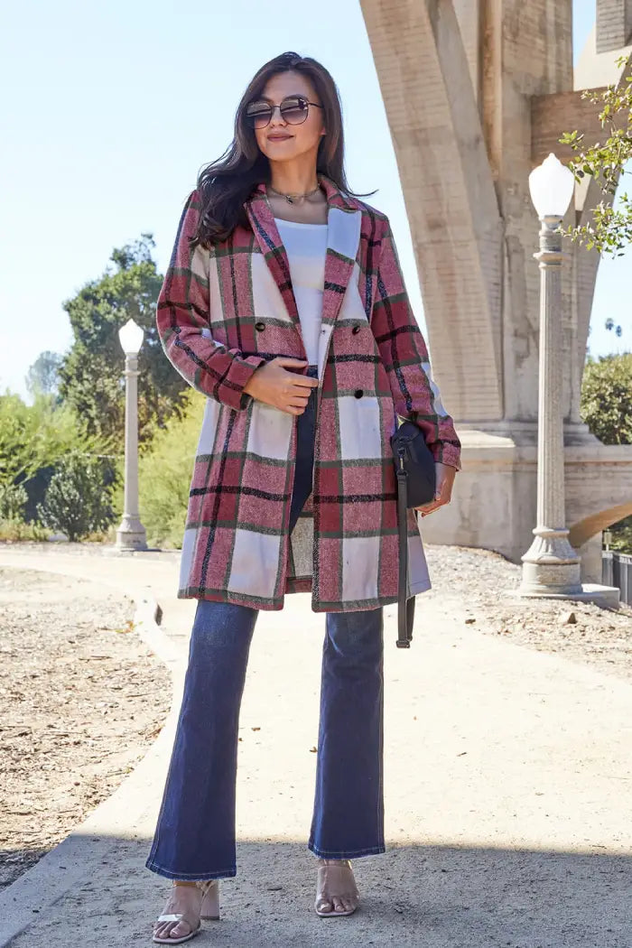 Full-length view of a woman in a pink and green plaid wool coat paired with flared jeans, heels, and a black crossbody bag outdoors.