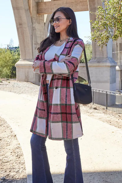 Woman in a pink and green plaid wool coat paired with flared jeans, a white top, and a black crossbody bag near an arched bridge.