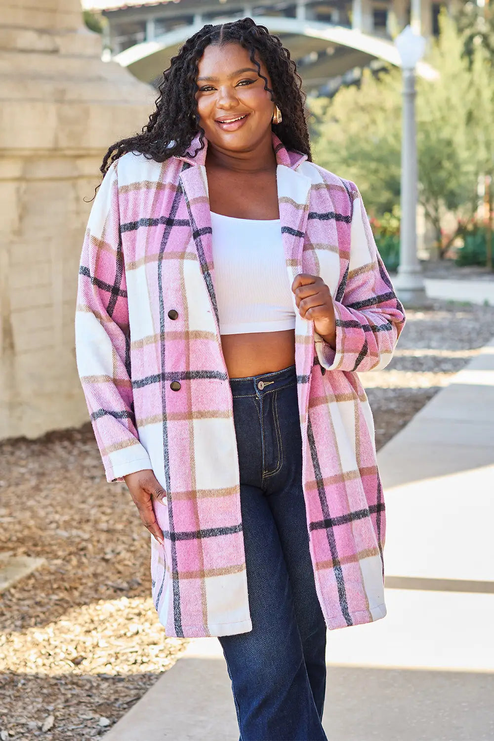 Plus-size woman in a pink and white plaid wool coat paired with a white crop top and dark blue jeans outdoors.