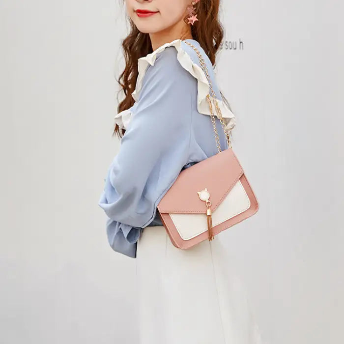 Close-up of a model wearing a pink crossbody bag with gold chain and cat charm paired with a light blue blouse.