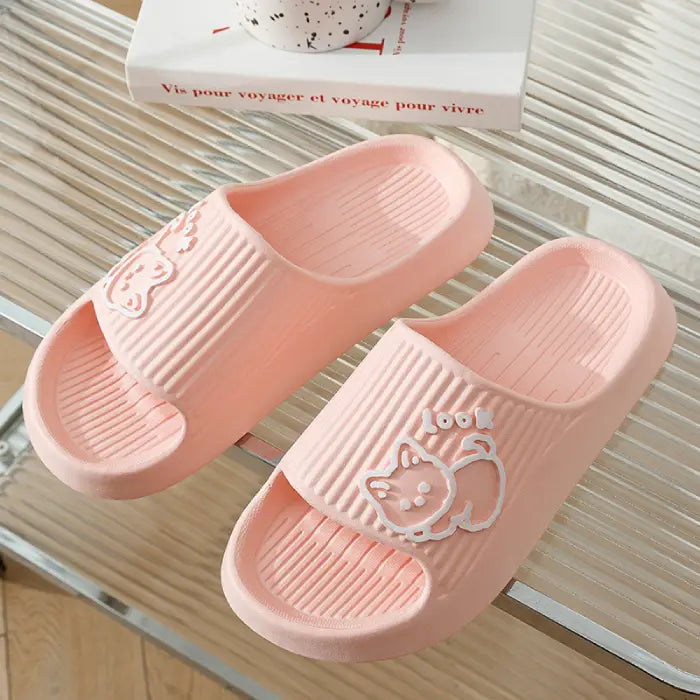 : Pair of pink bathroom slides with embossed cat design displayed on striped surface with French book in background