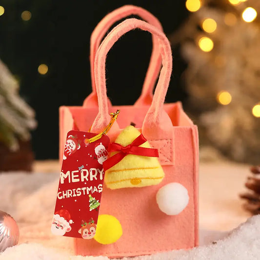 Pink Christmas gift bag with a yellow bell ornament, pom-poms, and a "Merry Christmas" tag.