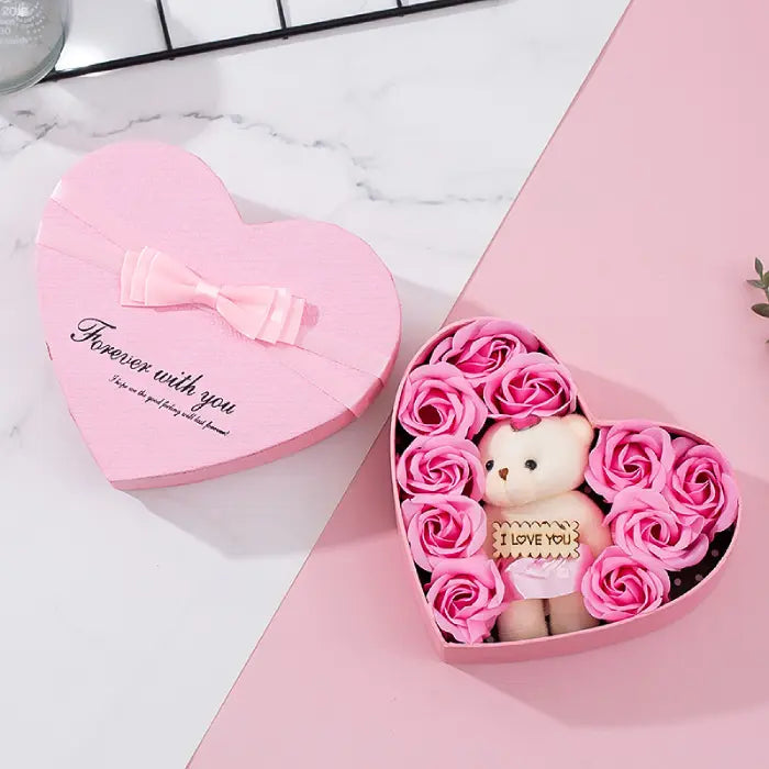 Open pink heart-shaped gift box with teddy bear and pink artificial roses, perfect for Valentine’s Day.