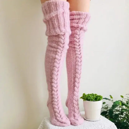 Pink knit thigh-high socks with cable pattern, white background, small potted plant in foreground