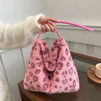 Pink leopard print faux fur handbag held by a hand wearing a soft white sweater for a cozy chic vibe.