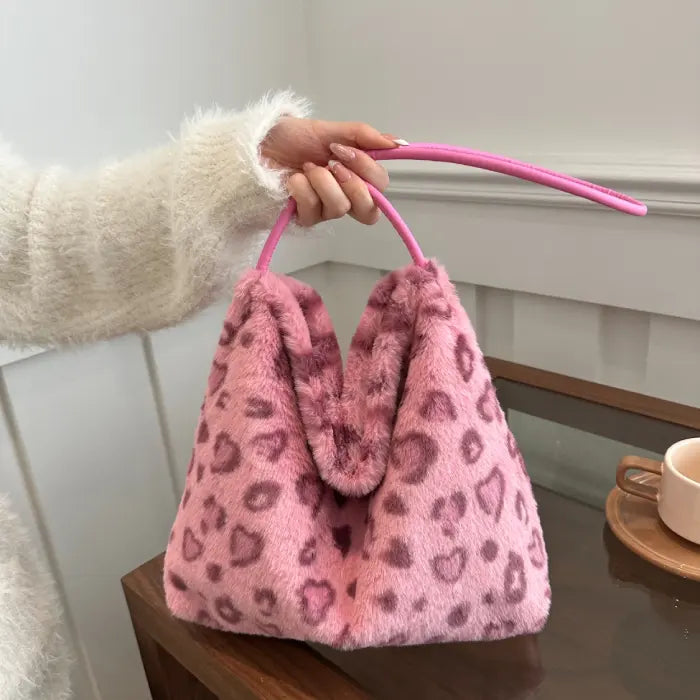 Pink leopard print faux fur handbag held by a hand wearing a soft white sweater for a cozy chic vibe.