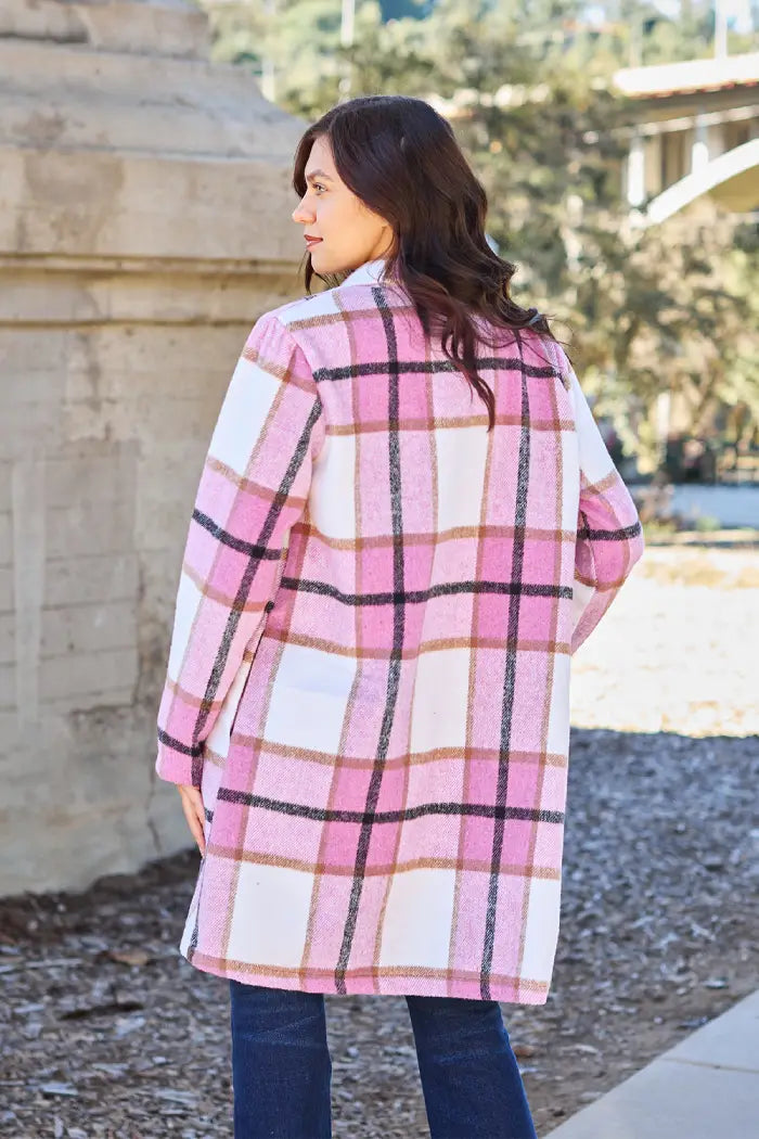 Woman showing the back view of a pink plaid wool coat, styled casually with jeans in an outdoor park setting.