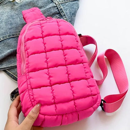 Hot pink puffer sling bag with quilted design, zipper closure and adjustable strap, displayed on denim jacket background