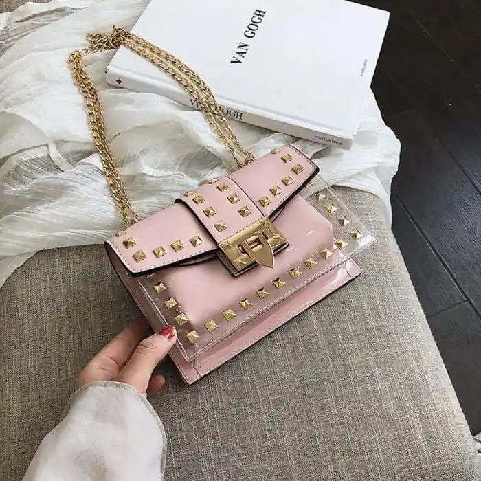 Pink leather handbag with gold studs and chain strap, displayed next to white fashion book on textured surface