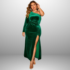 Plus size formal one shoulder dress photographed from side angle highlighting emerald velvet material, twist waist detail and leg slit.