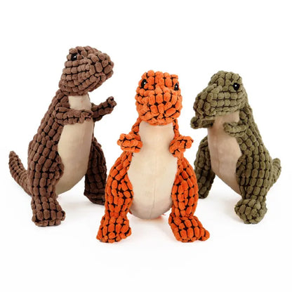 Three plush dinosaur dog toys in brown, orange, and green, with soft textured patterns and upright poses.