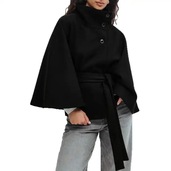 Poncho coat in black with wide sleeves, belted waist, and high neck on model.