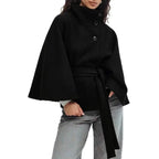 Poncho coat in black with wide sleeves, belted waist, and high neck on model.