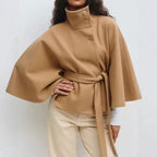 Camel poncho coat with asymmetrical button detail and tie waist, modeled with beige pants.