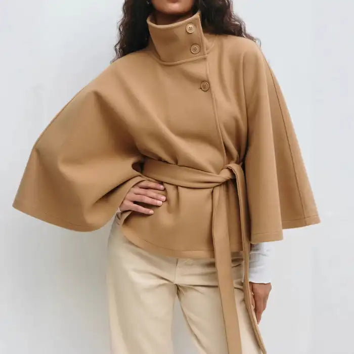 Camel poncho coat with asymmetrical button detail and tie waist, modeled with beige pants.
