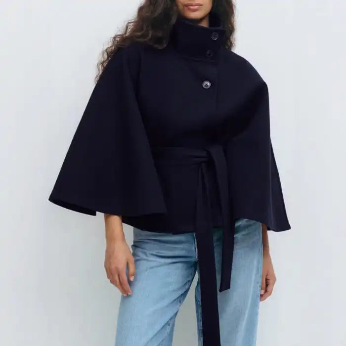 Navy poncho coat with belt and stand collar, worn over denim jeans for a modern outfit.