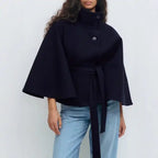 Navy poncho coat with belt and stand collar, worn over denim jeans for a modern outfit.
