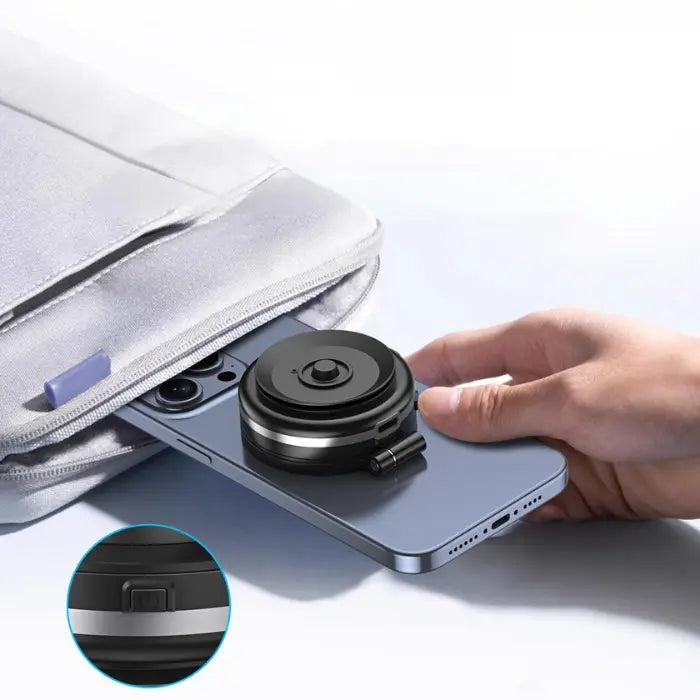 Small magnetic phone holder with power switch being placed on smartphone, next to laptop bag for easy portability