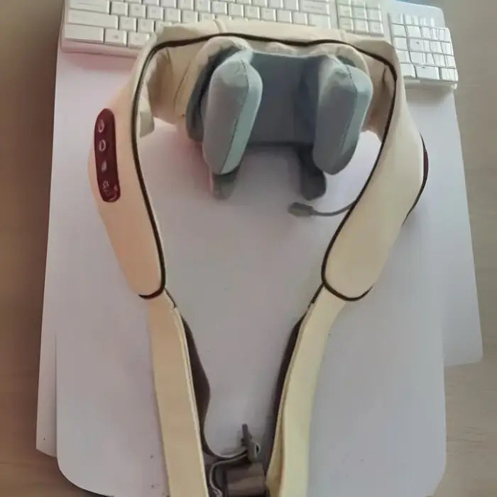 Cream-colored electronic neck and shoulder massager with control buttons displayed on white desk surface near keyboard