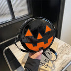 Glossy black Pumpkin Head Purse with orange pumpkin face held in hand near tabletop decor.
