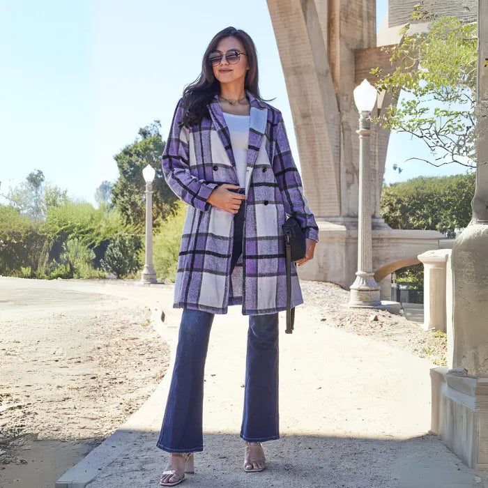Long purple checkered coat paired with flared jeans and neutral heels in outdoor architectural setting