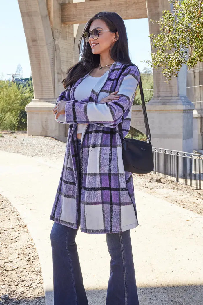 Woman wearing a purple plaid wool coat, styled with flared jeans, a white top, and a black crossbody bag outdoors.