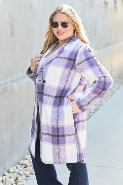 Back view of a woman with blonde curls wearing a purple plaid wool coat paired with dark jeans in a minimalist outdoor setting.