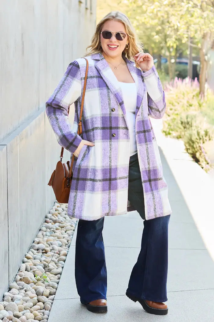 Plus-size woman wearing a purple plaid wool coat paired with flared jeans, a white top, and sunglasses on a sunny day.