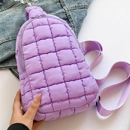 Purple quilted sling bag with zipper closure and adjustable strap, displayed on denim jacket background