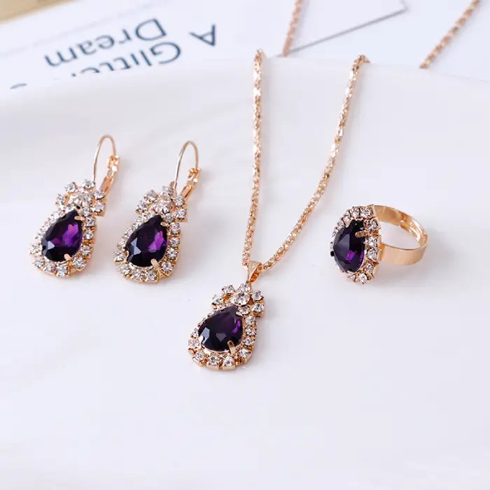 Purple teardrop gemstone jewelry set featuring necklace, earrings, and ring with crystal details in gold.