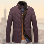 Quilted insulated jacket in maroon with fur collar and warm lining shown against a soft city backdrop.