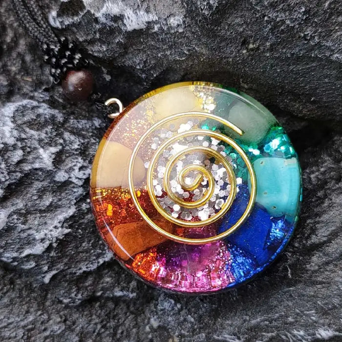 Colorful chakra healing pendant with gold spiral design and vibrant stones on a textured background.