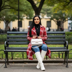 Red belted trench styled while seated in a park, featuring a plaid coat worn with boots for relaxed winter outfit ideas.