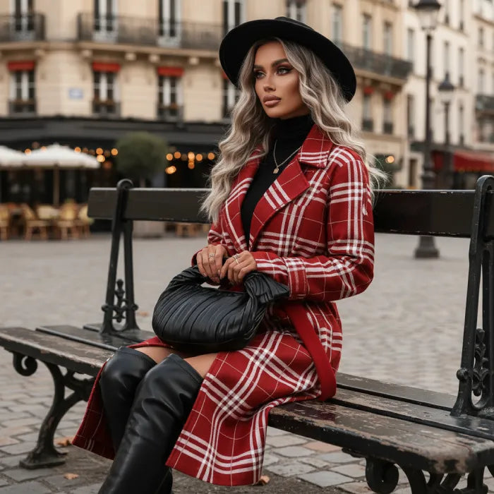 Red belted trench styled on a woman seated on a city bench, showcasing a plaid coat with boots for elegant winter outfits.