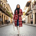 Red belted trench worn by a woman walking a cobblestone street, plaid design styled with boots for elegant winter outfits.