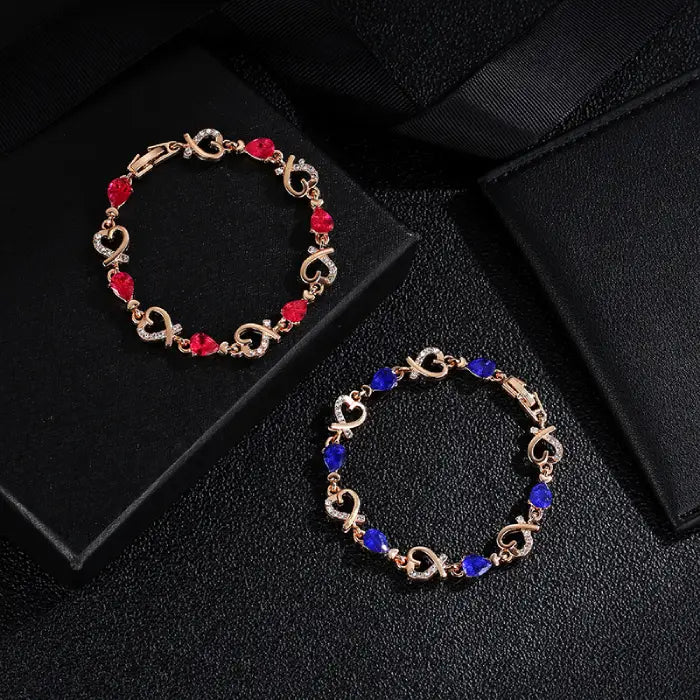 Display of red and blue gemstone bracelets with heart designs on a luxurious black setting.