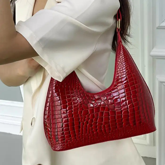 Person in white outfit carrying glossy red crocodile-embossed shoulder bag