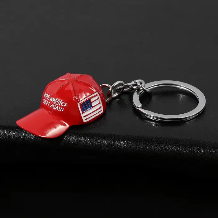 Red hat keychain with "Make America Great Again" text and USA flag displayed on a dark black surface.