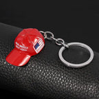 Red hat keychain with "Make America Great Again" text and USA flag on black leather background.