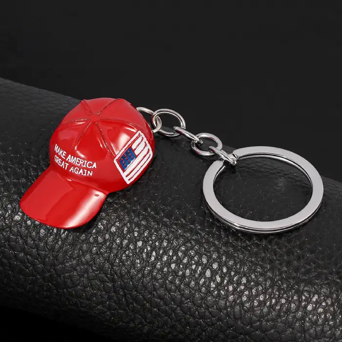 Red hat keychain with "Make America Great Again" text and USA flag on black leather background.