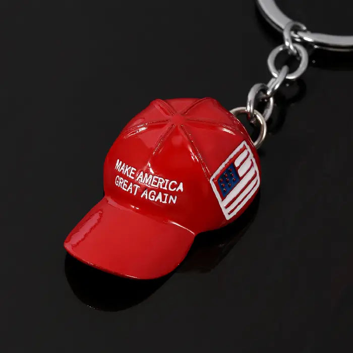 Closeup of red hat keychain with "Make America Great Again" text and USA flag on dark reflective background.